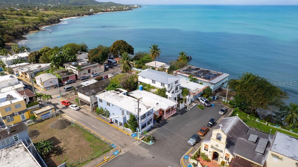 An aerial view shows a coastal neighborhood with houses, a church, and a beach — 112 CALLE MUÑOZ RIVERA, VIEQUES, PR
