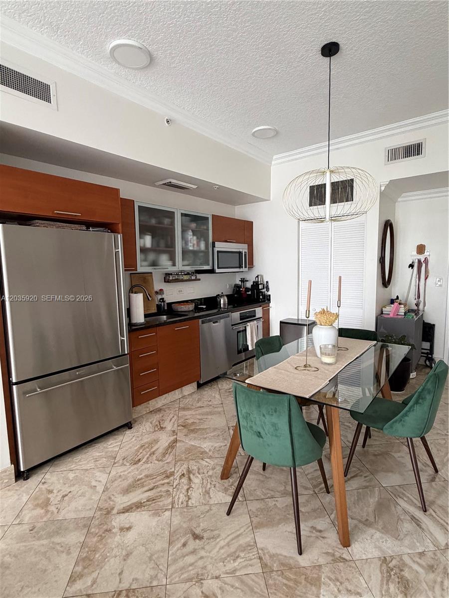 A kitchen features stainless steel appliances, wood cabinets, and a glass dining table with chairs — 3470 E Coast Ave # H1206, Miami FL 33137, MIAMI, FL