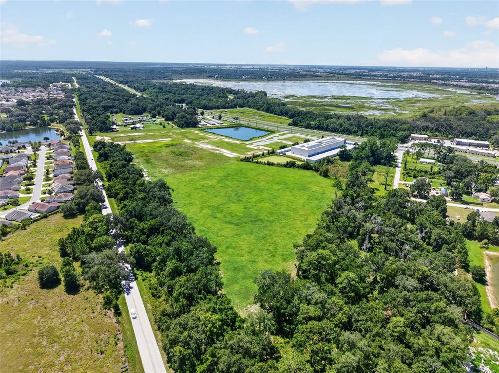An aerial view shows a large, grassy vacant lot bordered by trees, roads, and buildings — 0 COUNTY ROAD 44 A, WILDWOOD, FL
