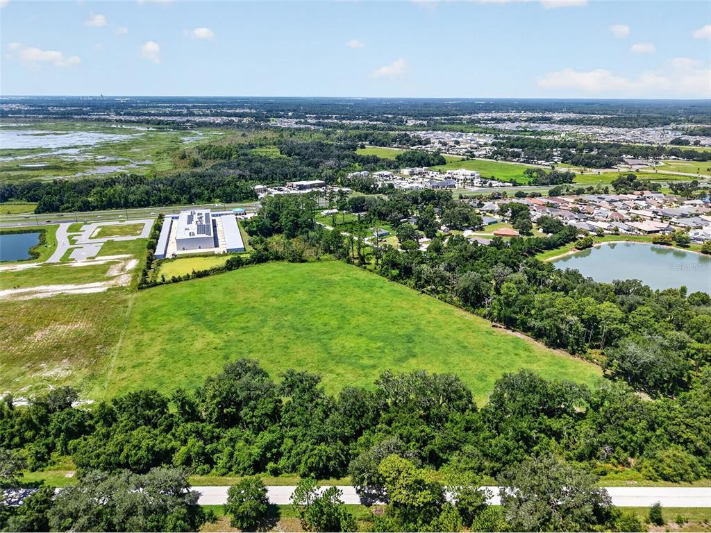 An aerial view shows a large, grassy vacant lot bordered by trees and nearby development — 0 COUNTY ROAD 44 A, WILDWOOD, FL