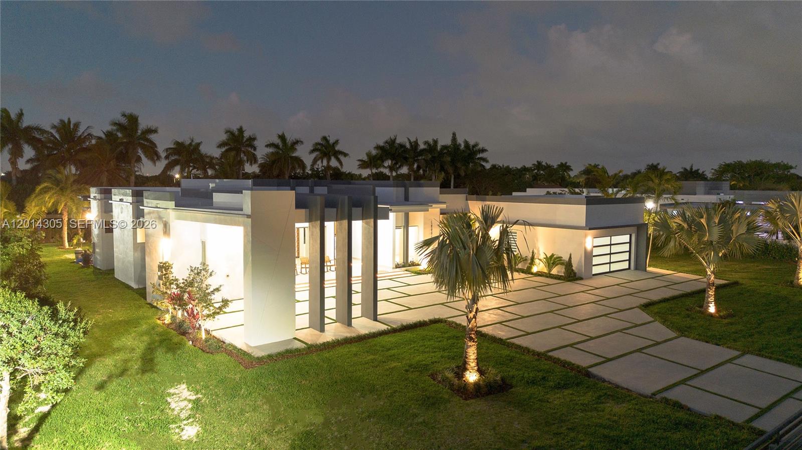 An exterior view of a modern, flat-roofed house at night with a paved driveway — 13231 SW 220 ST, Miami FL 33170, MIAMI, FL