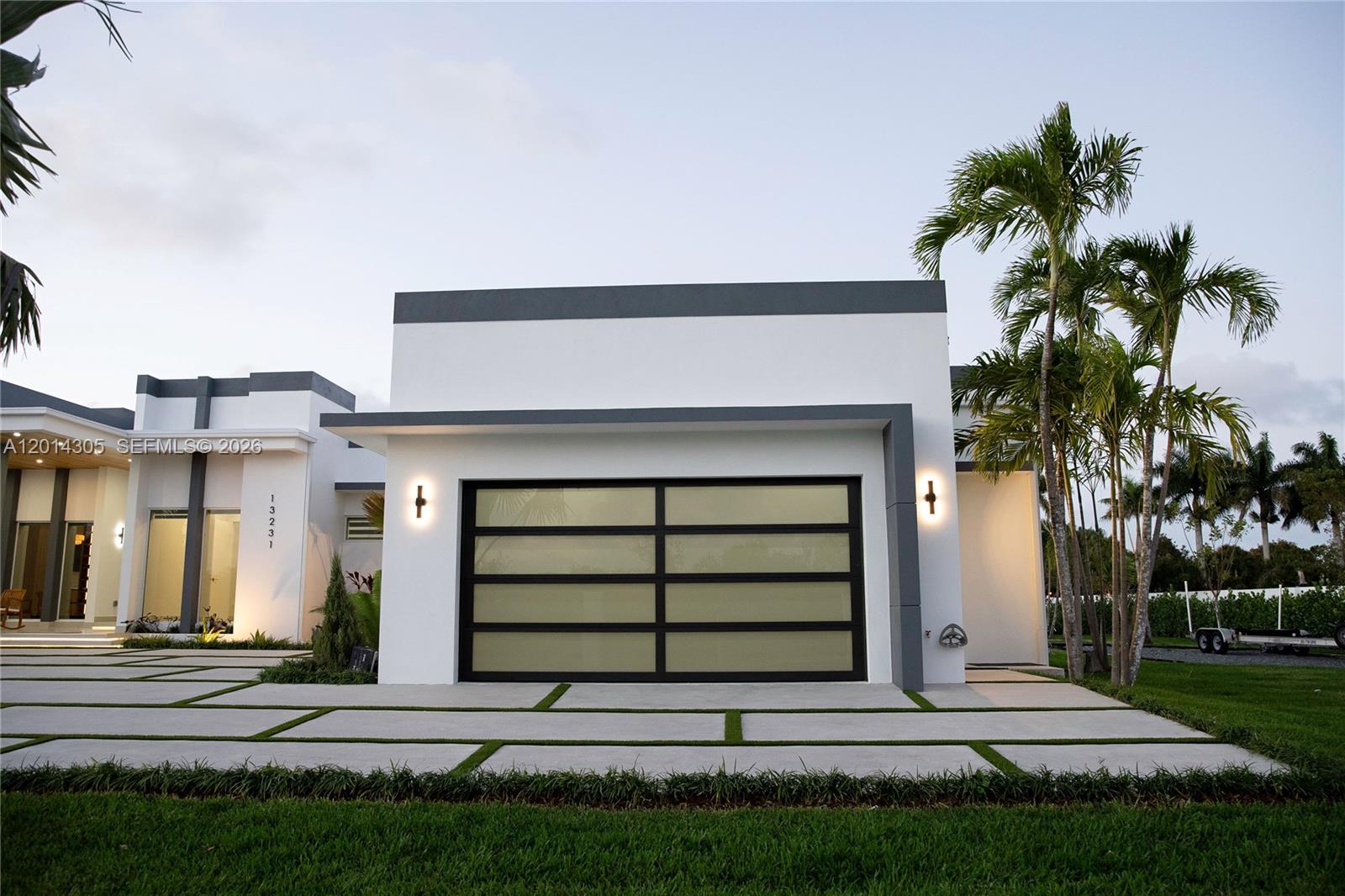 A modern white house exterior features a glass garage door and a paved driveway — 13231 SW 220 ST, Miami FL 33170, MIAMI, FL