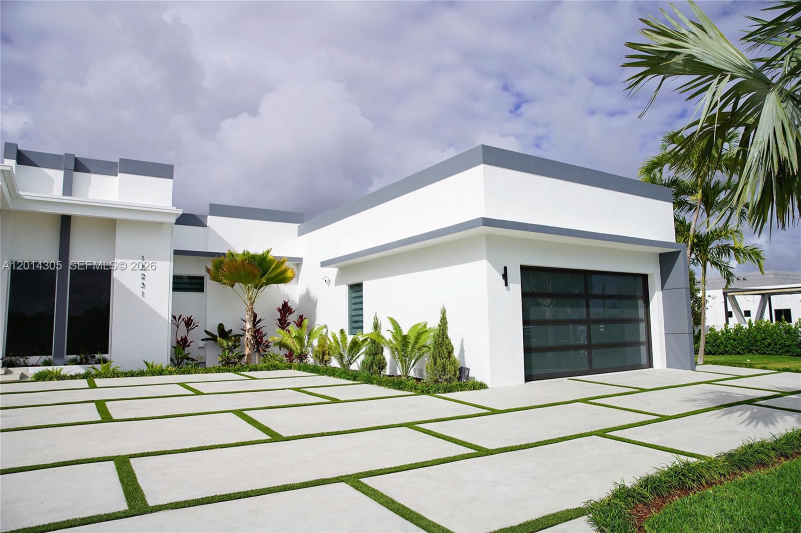 A modern white house features a glass garage door and a geometric concrete driveway — 13231 SW 220 ST, Miami FL 33170, MIAMI, FL