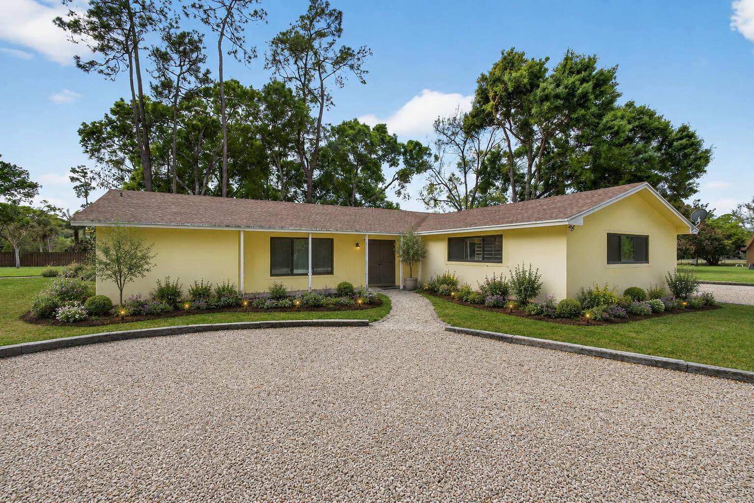 A yellow single-story house with a gravel driveway and landscaped garden under a blue sky — 749 W Rambling Drive, Wellington FL 33414, WELLINGTON, FL