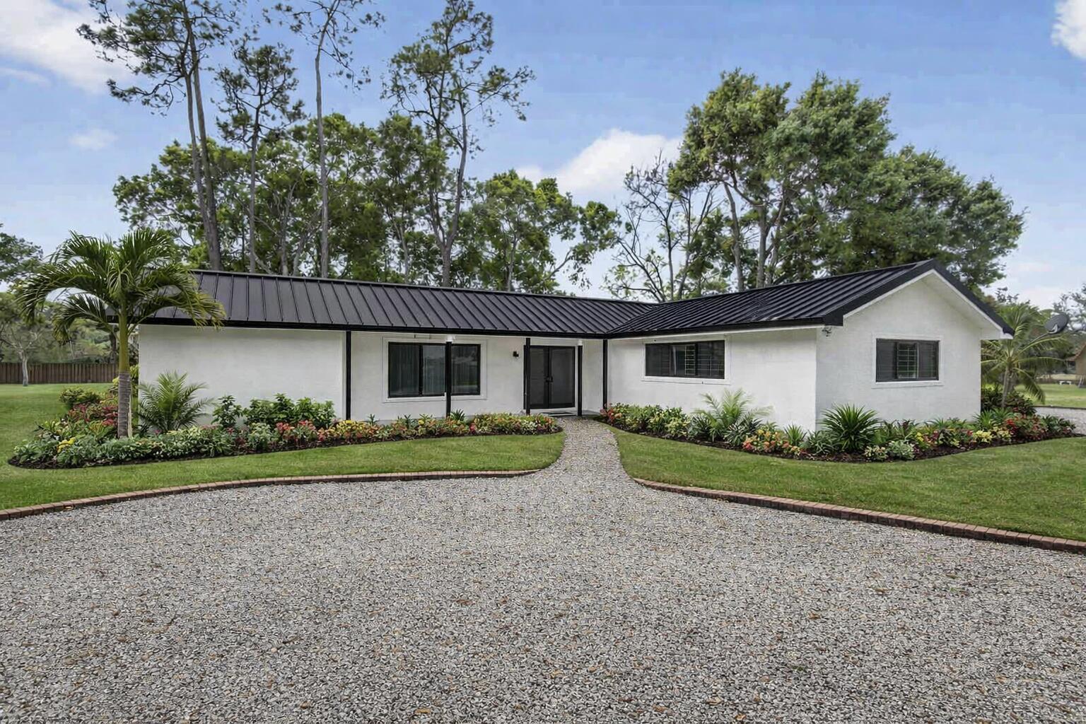 A white, single-story house with a black metal roof and a gravel driveway — 749 W Rambling Drive, Wellington FL 33414, WELLINGTON, FL