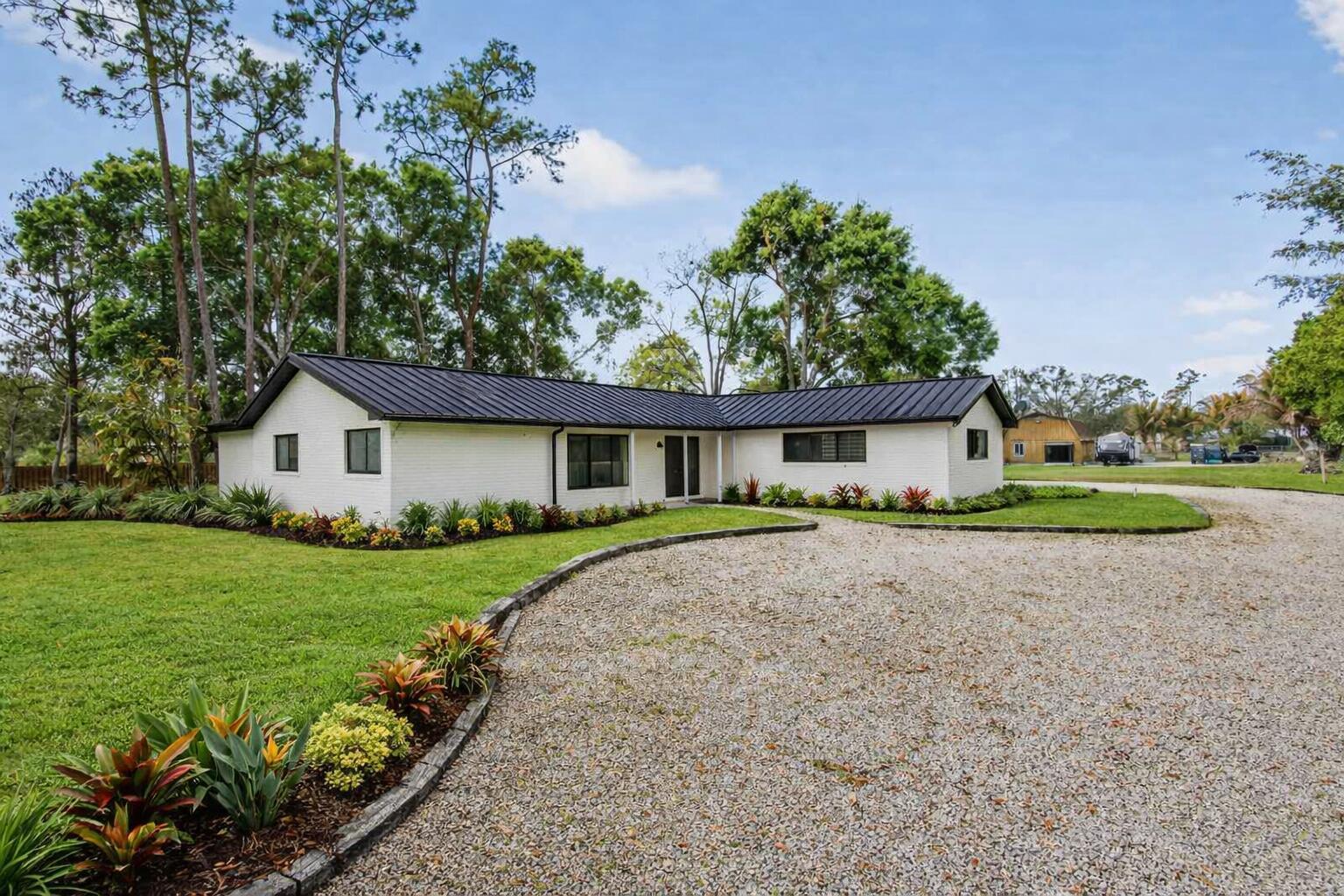 A white brick ranch-style house with a black metal roof and a gravel driveway — 749 W Rambling Drive, Wellington FL 33414, WELLINGTON, FL