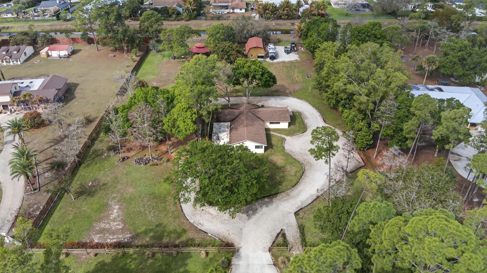An aerial view shows a house with a circular gravel driveway on a wooded lot — 749 W Rambling Drive, Wellington FL 33414, WELLINGTON, FL
