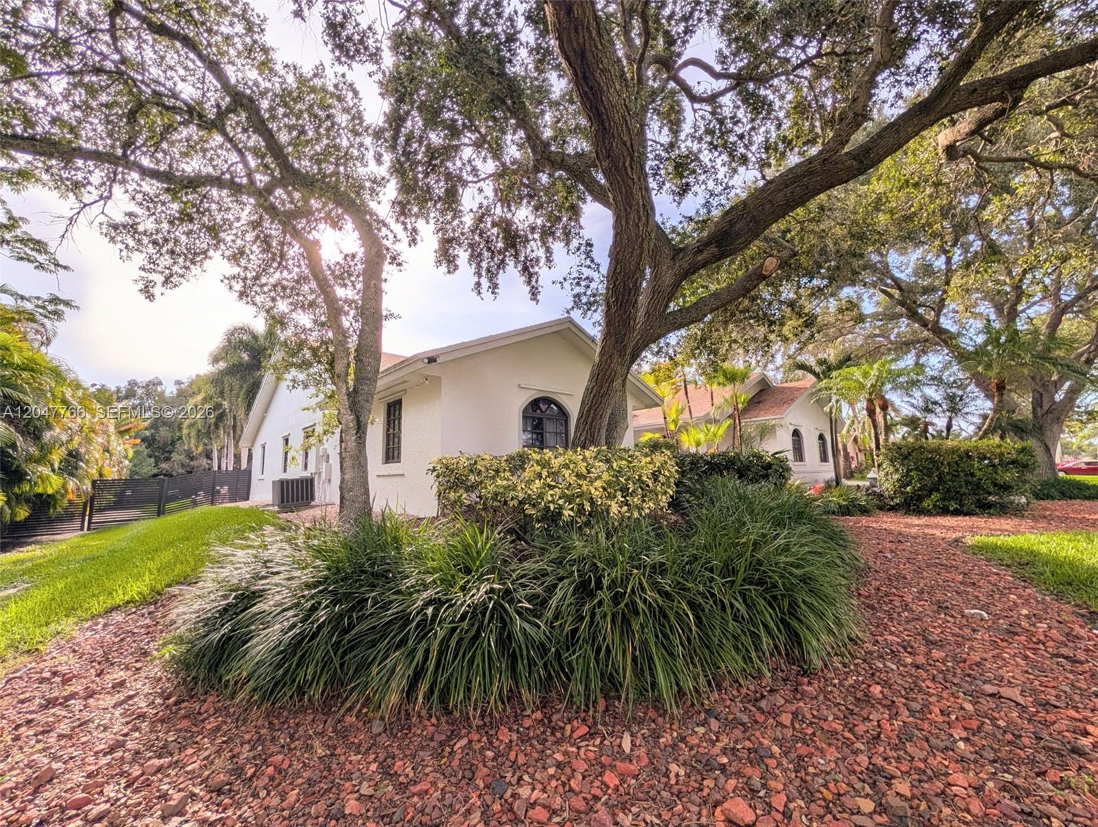 A white house with arched windows is surrounded by mature trees and landscaped garden beds — 5131 SW 201st Ter, Southwest Ranches FL 33332, SOUTHWEST RANCHES, FL