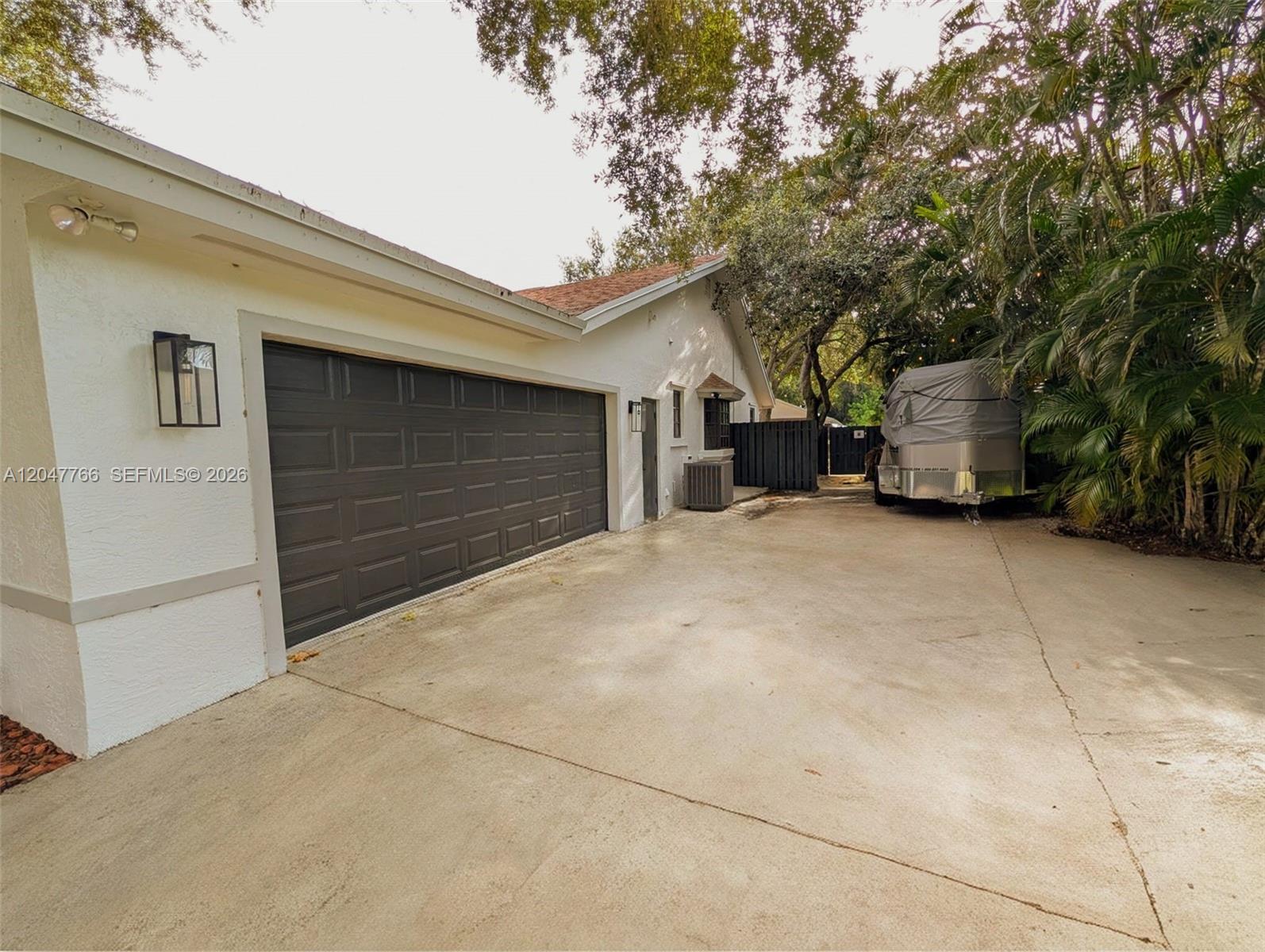 A white house features a dark garage door, a concrete driveway, and a parked trailer — 5131 SW 201st Ter, Southwest Ranches FL 33332, SOUTHWEST RANCHES, FL