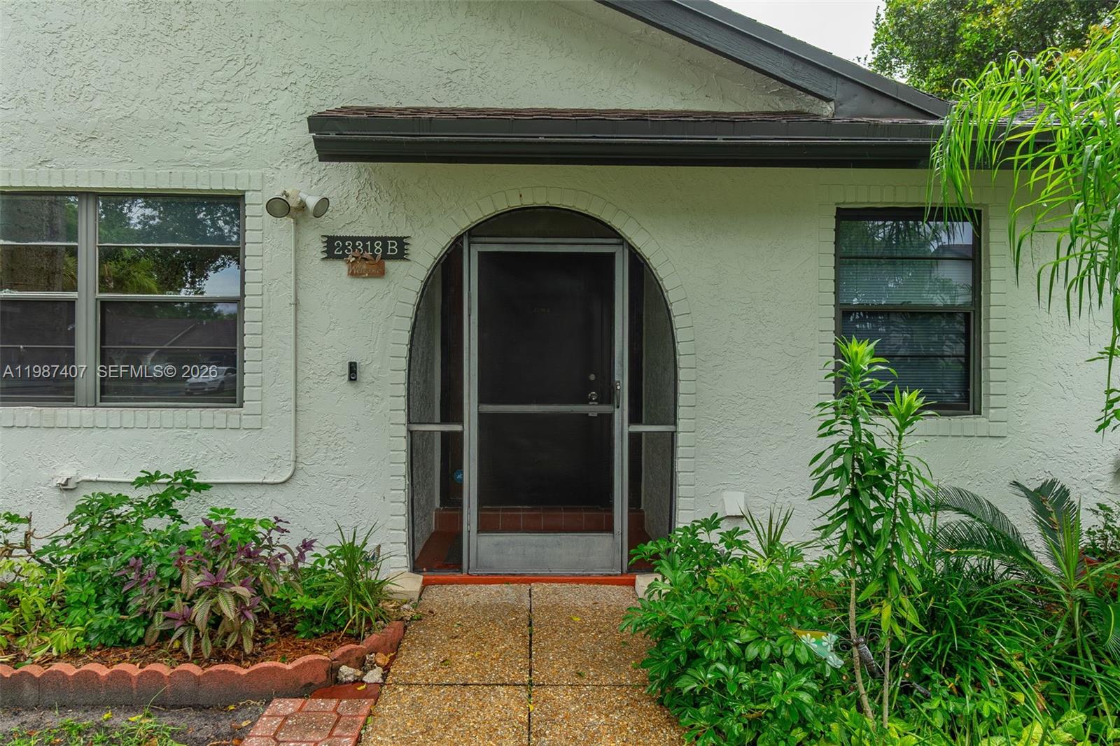The exterior of a house features a stucco facade, an arched entryway, and a screen door — 23318 SW 55th Way # B, Boca Raton FL 33433, BOCA RATON, FL