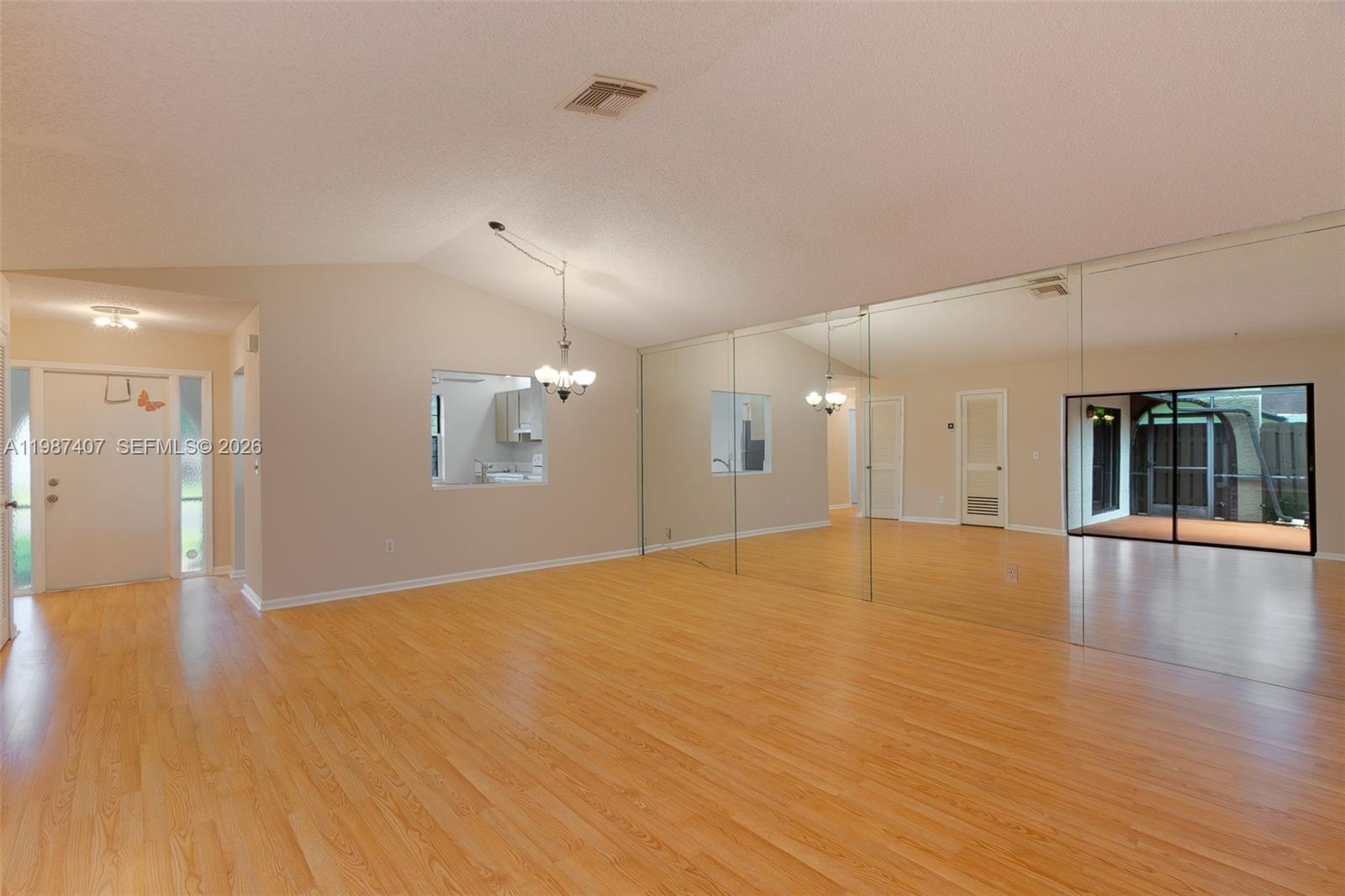A living room features light wood flooring, a vaulted ceiling, and a large mirrored wall — 23318 SW 55th Way # B, Boca Raton FL 33433, BOCA RATON, FL