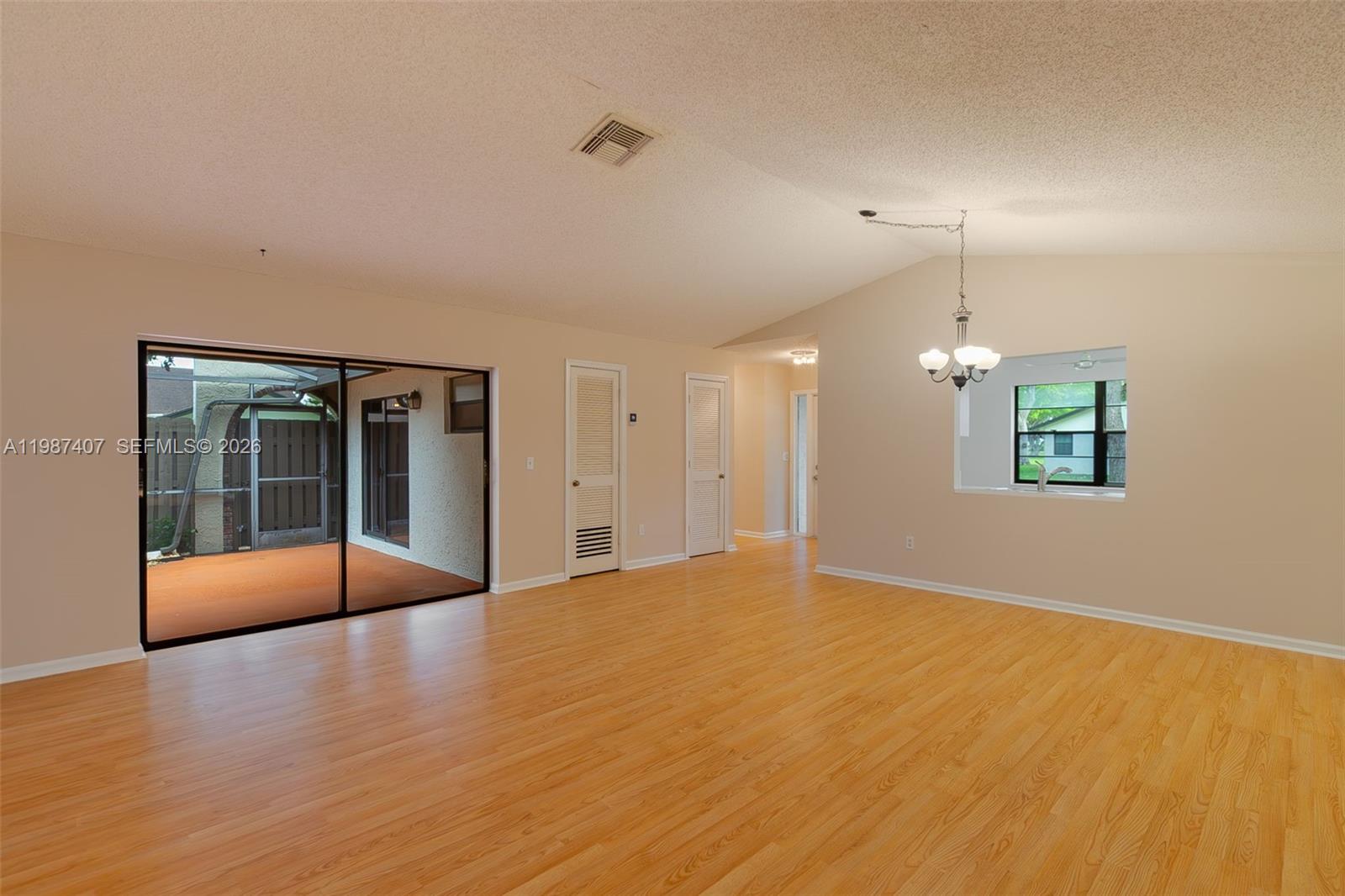 An empty living room features light wood flooring, a sliding glass door, and a chandelier — 23318 SW 55th Way # B, Boca Raton FL 33433, BOCA RATON, FL