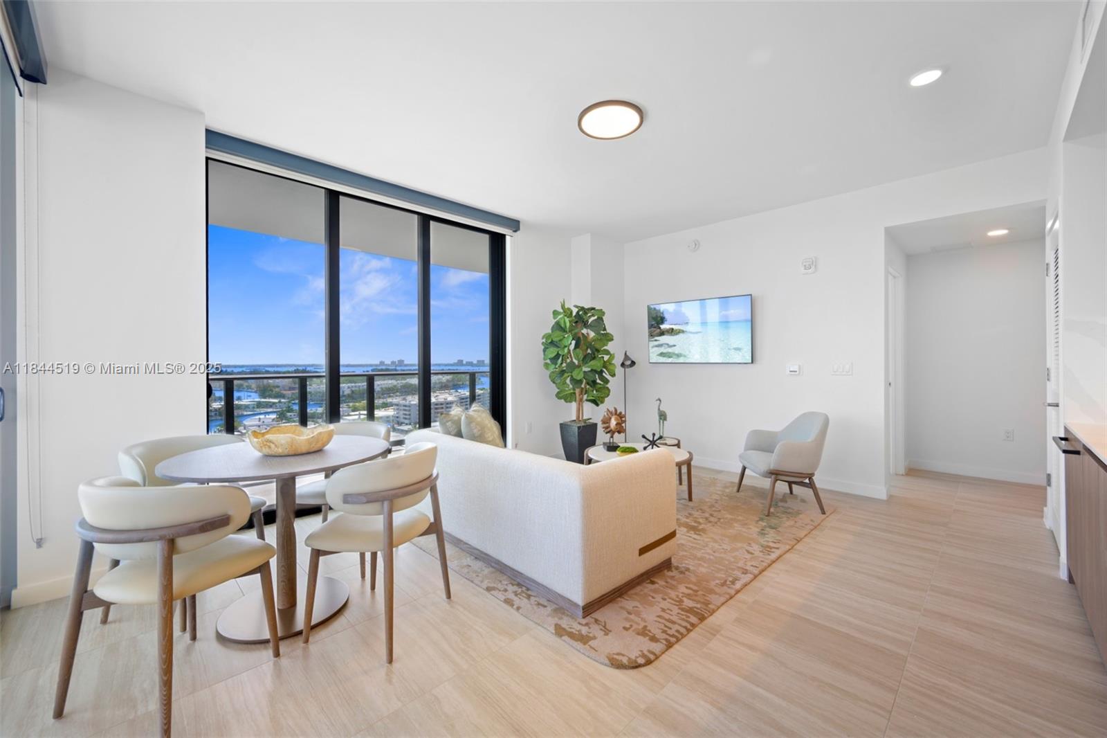A modern living and dining area features light wood flooring, a sofa, and floor-to-ceiling windows — 580 72nd St # 1210, Miami Beach FL 33141, MIAMI BEACH, FL