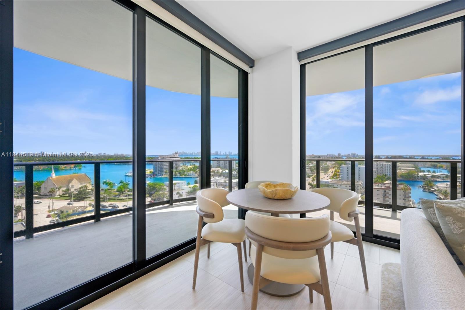 A dining area with a round table and chairs features floor-to-ceiling windows overlooking a bay — 580 72nd St # 1210, Miami Beach FL 33141, MIAMI BEACH, FL