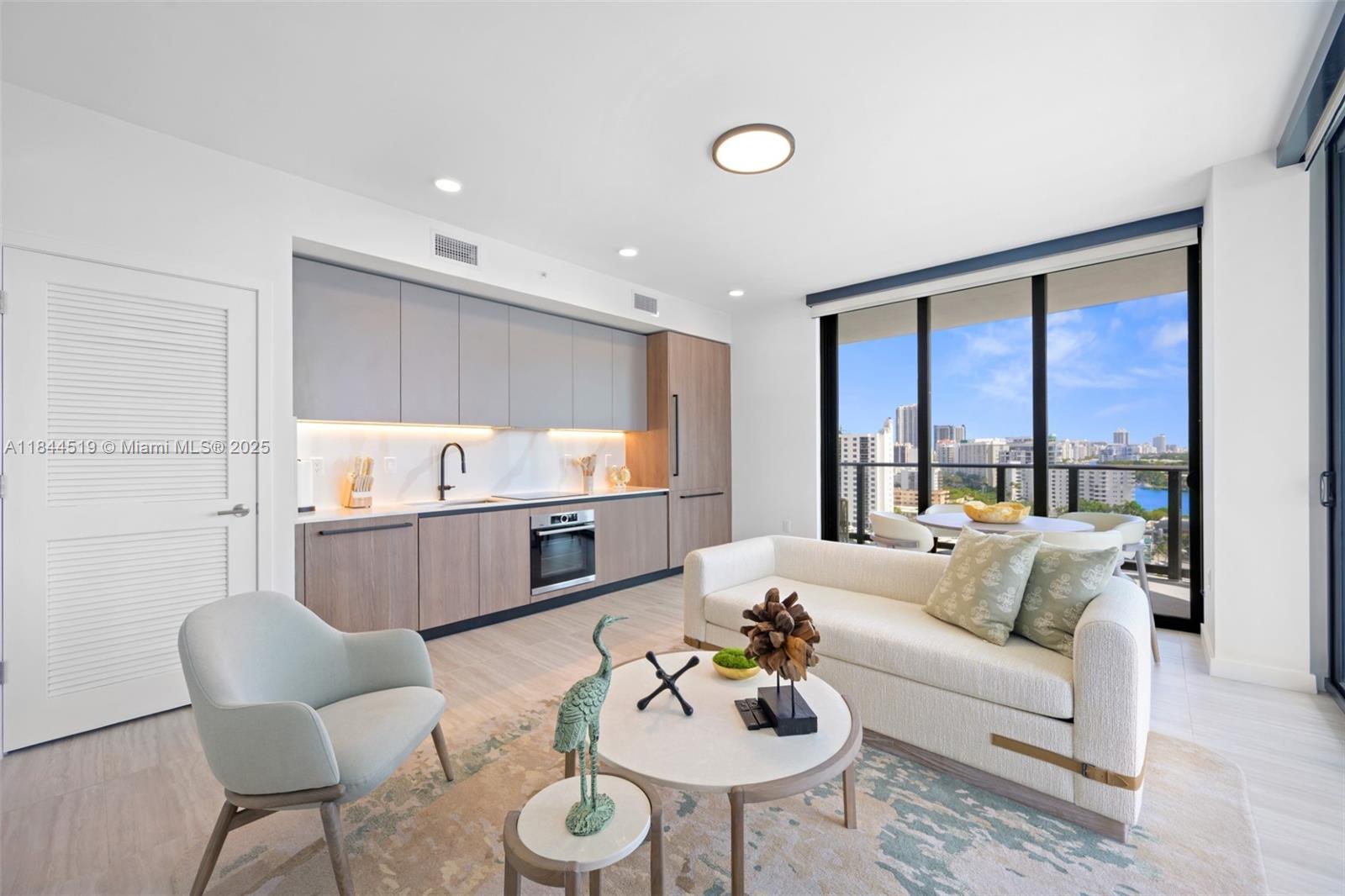 A modern open-plan living room and kitchen featuring light wood cabinetry and floor-to-ceiling windows — 580 72nd St # 1210, Miami Beach FL 33141, MIAMI BEACH, FL