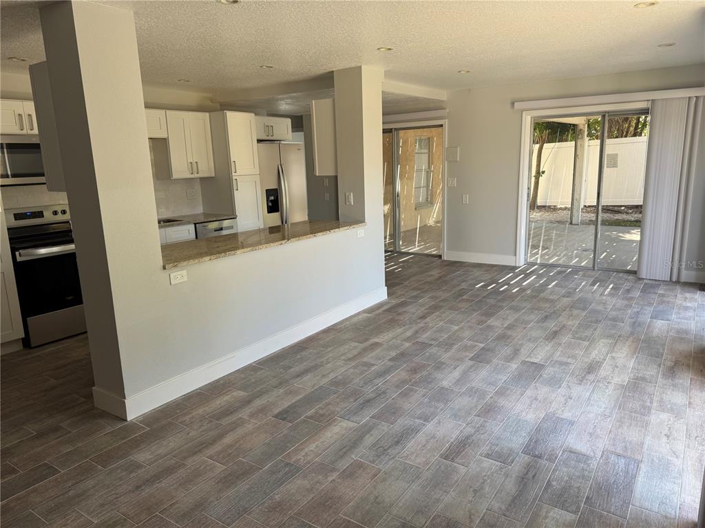 A kitchen with white cabinets and granite countertops overlooks a living area with tile flooring — 1209 1ST STREET, INDIAN ROCKS BEACH, FL