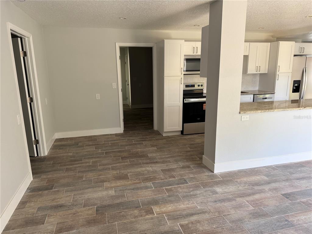 A kitchen with white cabinets and wood-look tile flooring opens to a hallway and room — 1209 1ST STREET, INDIAN ROCKS BEACH, FL