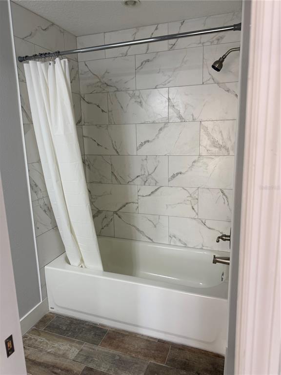 A bathroom features a white bathtub with a marble-patterned tile surround and a shower curtain — 1209 1ST STREET, INDIAN ROCKS BEACH, FL