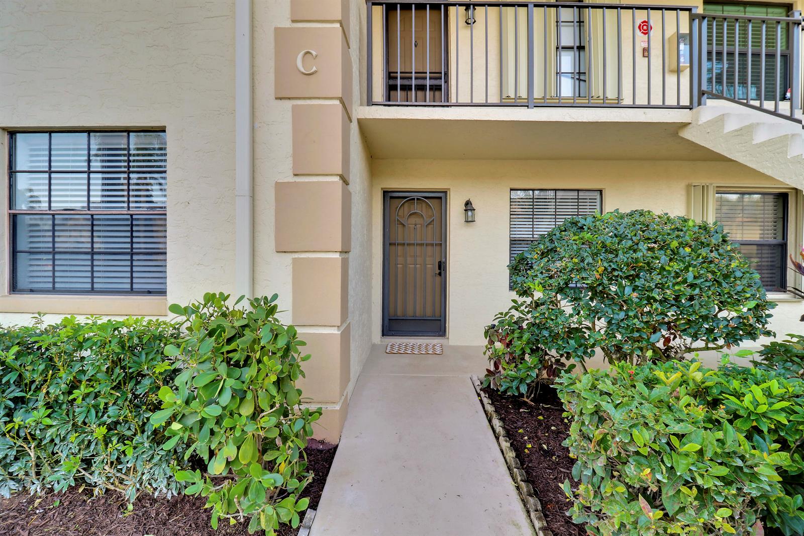 A ground-level apartment entrance with a screen door, concrete walkway, and surrounding landscaping — 1001 Pinecrest Circle # C, Jupiter FL 33458, JUPITER, FL