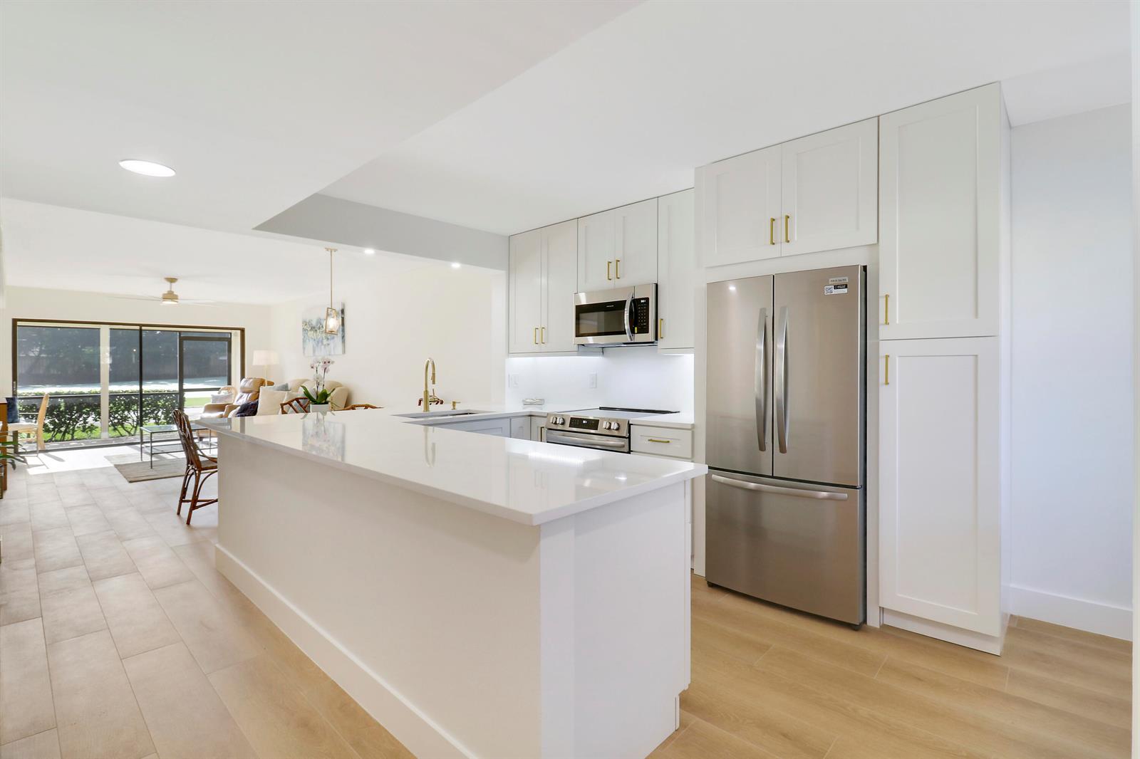 A modern kitchen features white cabinets, stainless steel appliances, and a quartz-topped breakfast bar — 1001 Pinecrest Circle # C, Jupiter FL 33458, JUPITER, FL