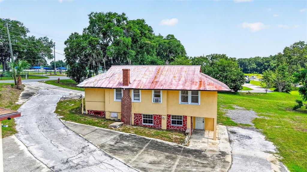 An exterior view of a two-story yellow house with a red metal roof — 2766 US HIGHWAY 441/27 HIGHWAY, FRUITLAND PARK, FL