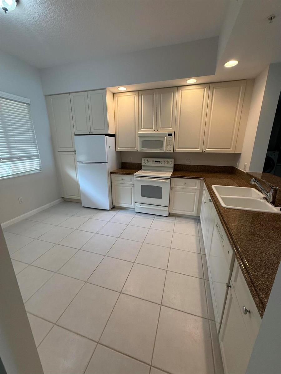 A kitchen features white cabinetry, white appliances, and brown granite countertops over light tile flooring — 4 Harbour Isle Drive E Unit 204, Fort Pierce FL 34949, FORT PIERCE, FL