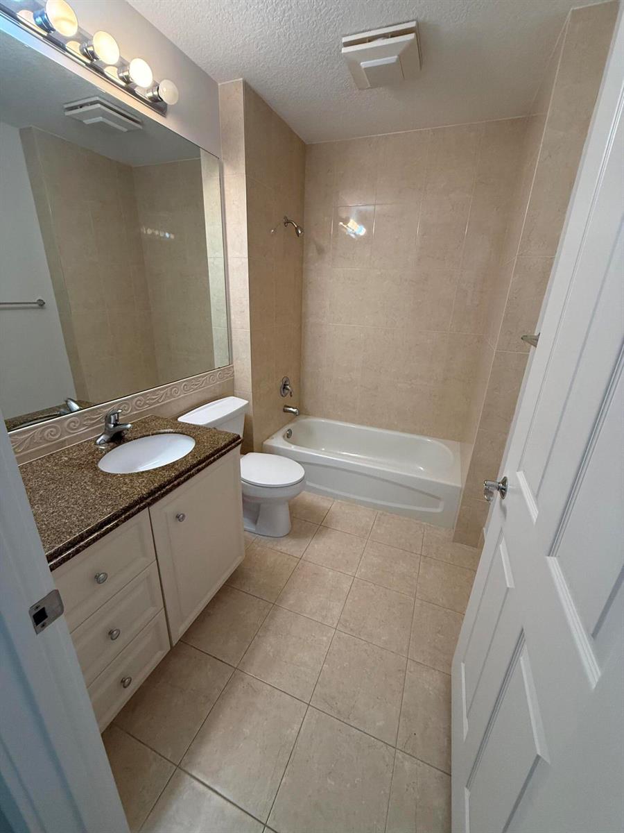 A bathroom features a vanity with a granite countertop, a toilet, and a tiled tub — 4 Harbour Isle Drive E Unit 204, Fort Pierce FL 34949, FORT PIERCE, FL