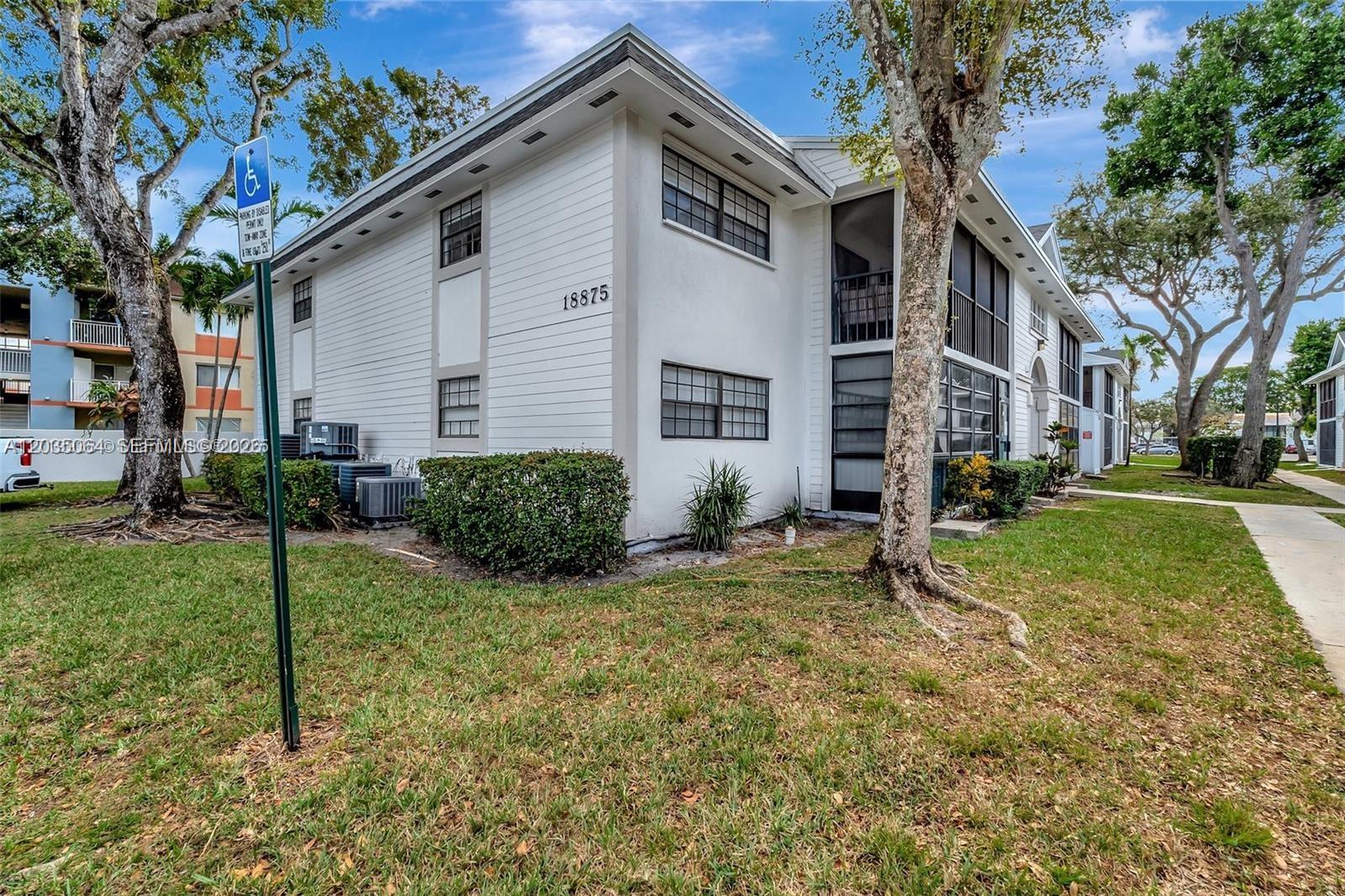 A two-story white apartment building with screened balconies stands on a grassy lawn — 18965 NW 62nd Ave # 210, Hialeah FL 33015, HIALEAH, FL
