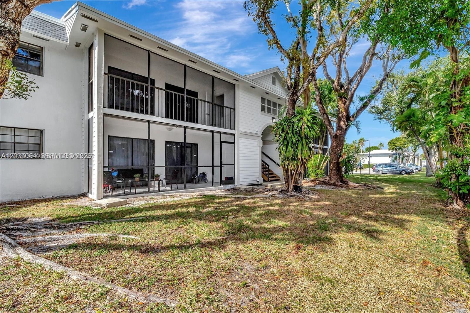 A two-story white building features screened-in balconies and patios overlooking a grassy lawn — 18965 NW 62nd Ave # 210, Hialeah FL 33015, HIALEAH, FL