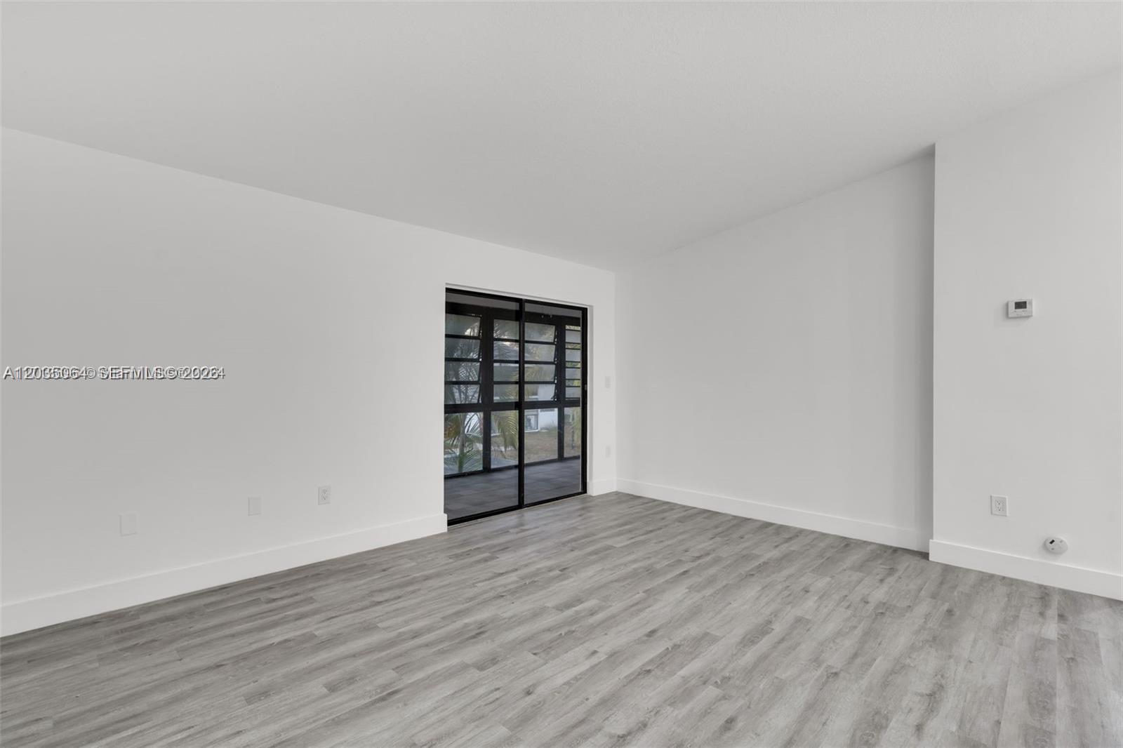 An empty room features light gray wood-look flooring, white walls, and a sliding glass door — 18965 NW 62nd Ave # 210, Hialeah FL 33015, HIALEAH, FL