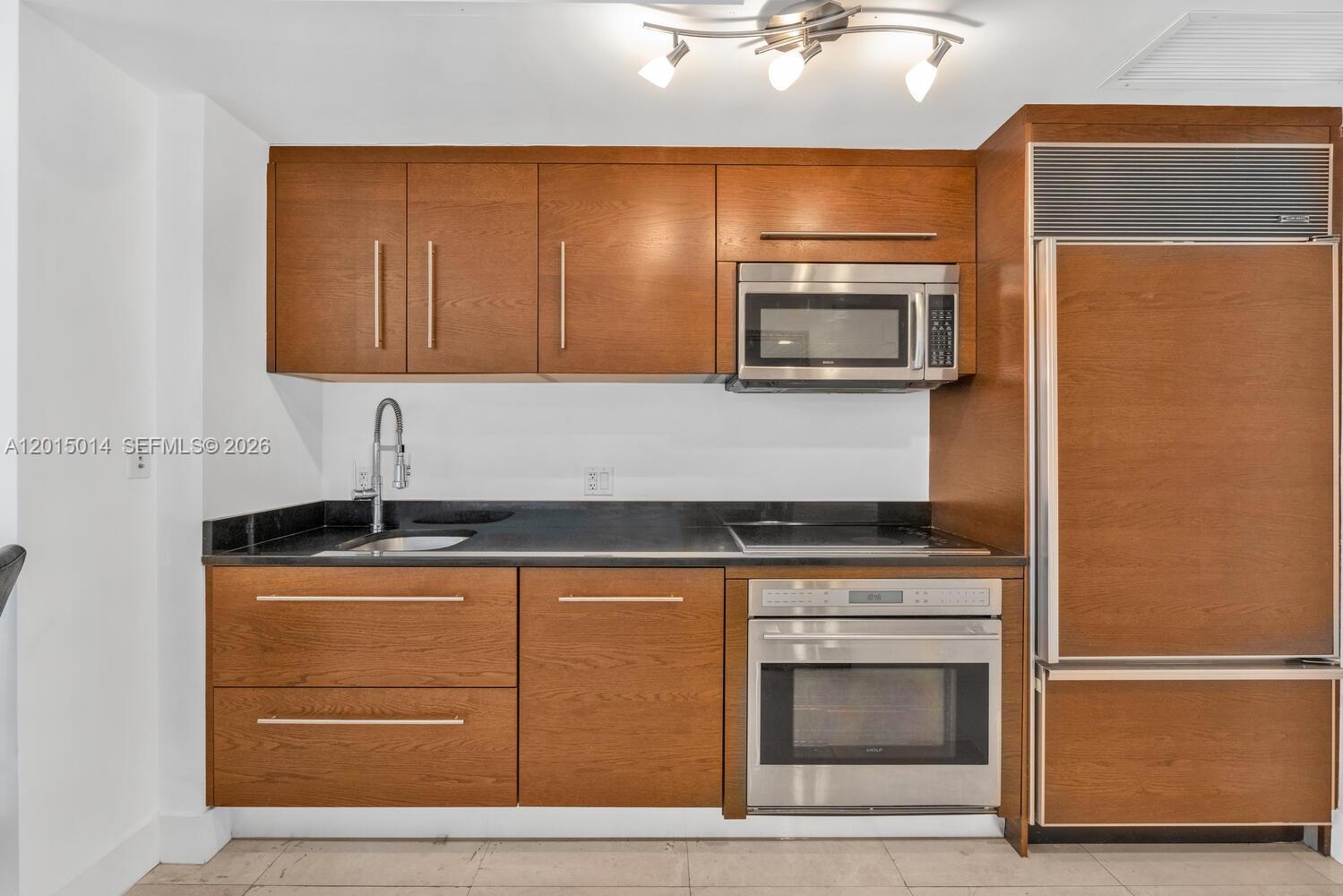 A kitchen features wood cabinets, stainless steel appliances, and a black countertop — 475 Brickell Ave # 2610, Miami FL 33131, MIAMI, FL