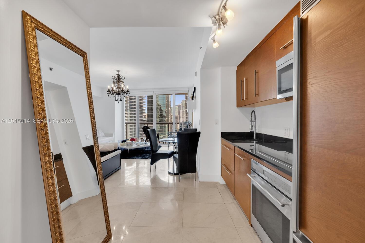A modern kitchen with wood cabinets and stainless steel appliances opens into a living area — 475 Brickell Ave # 2610, Miami FL 33131, MIAMI, FL