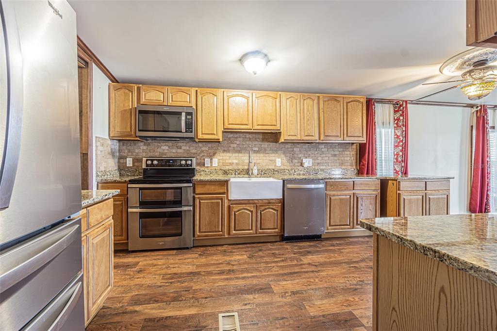 A kitchen with wood cabinets, stainless steel appliances, a farmhouse sink, and granite countertops — 34445 COUNTRYSIDE DRIVE, WESLEY CHAPEL, FL