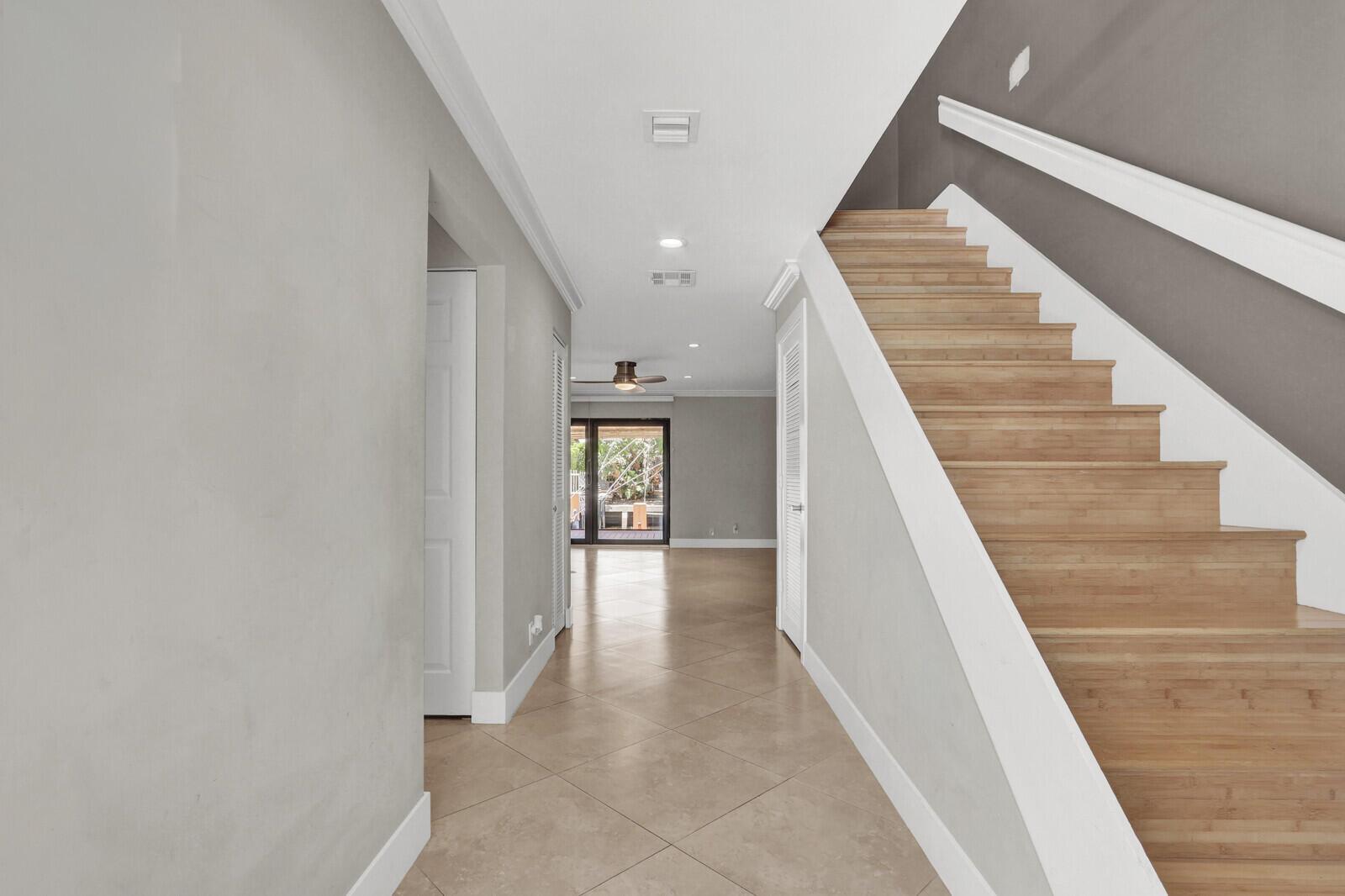 A hallway with tile flooring leads to a glass door, featuring a staircase with wooden treads — 611 NE 12th Terrace # 1, Boynton Beach FL 33435, BOYNTON BEACH, FL