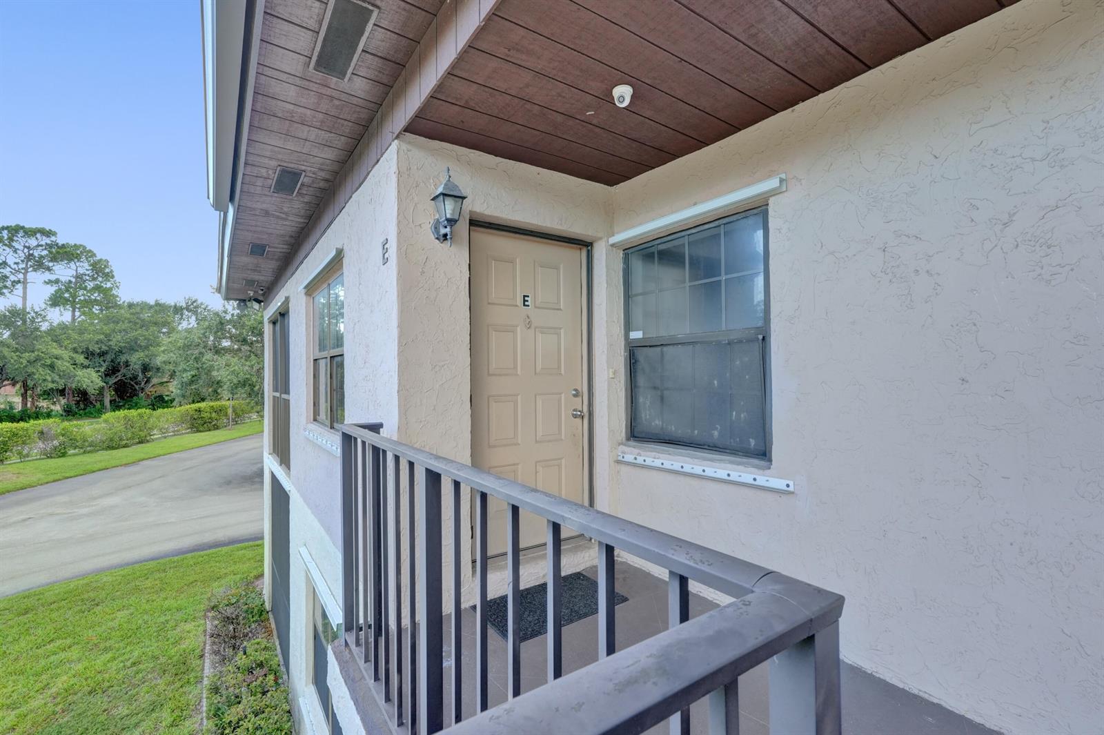 An exterior view of a second-story apartment balcony with a tan door marked E — 4225 S 57th Avenue, FL 33463, FL