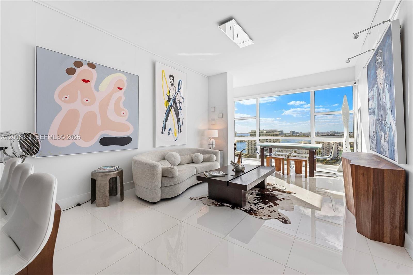 A modern living room features white tile floors, contemporary art, a curved sofa, and floor-to-ceiling windows — 6801 Collins Ave, Miami Beach FL 33141, MIAMI BEACH, FL