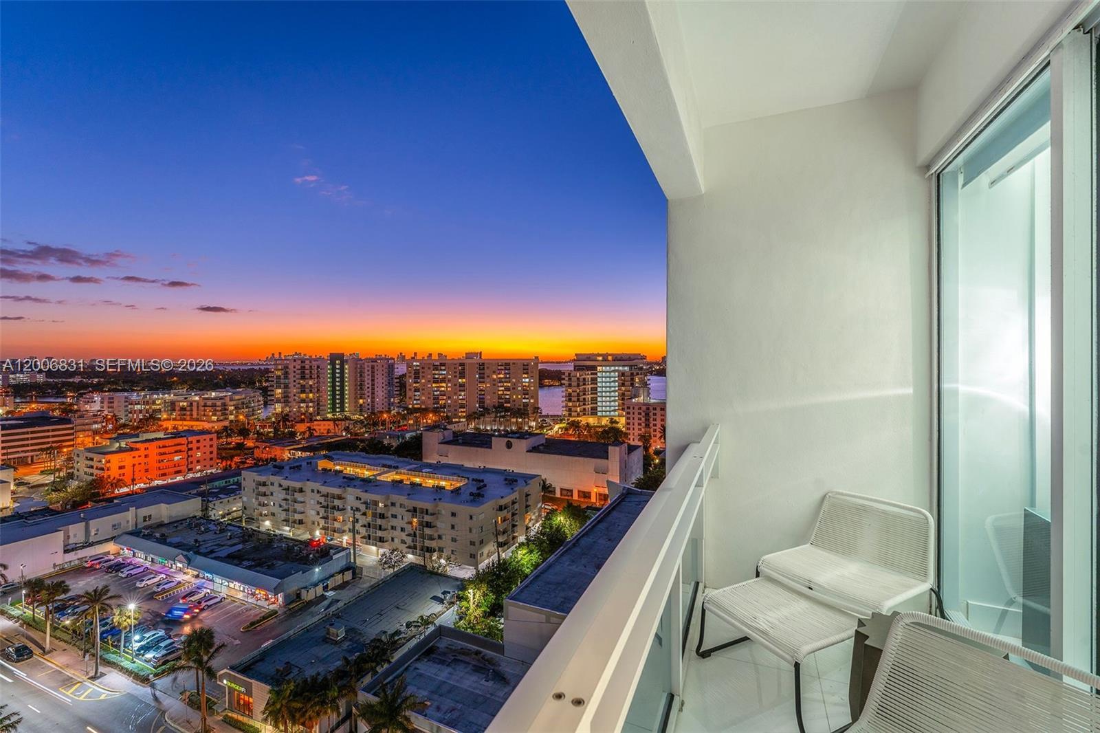 A balcony with white chairs overlooks a city skyline at sunset — 6801 Collins Ave, Miami Beach FL 33141, MIAMI BEACH, FL