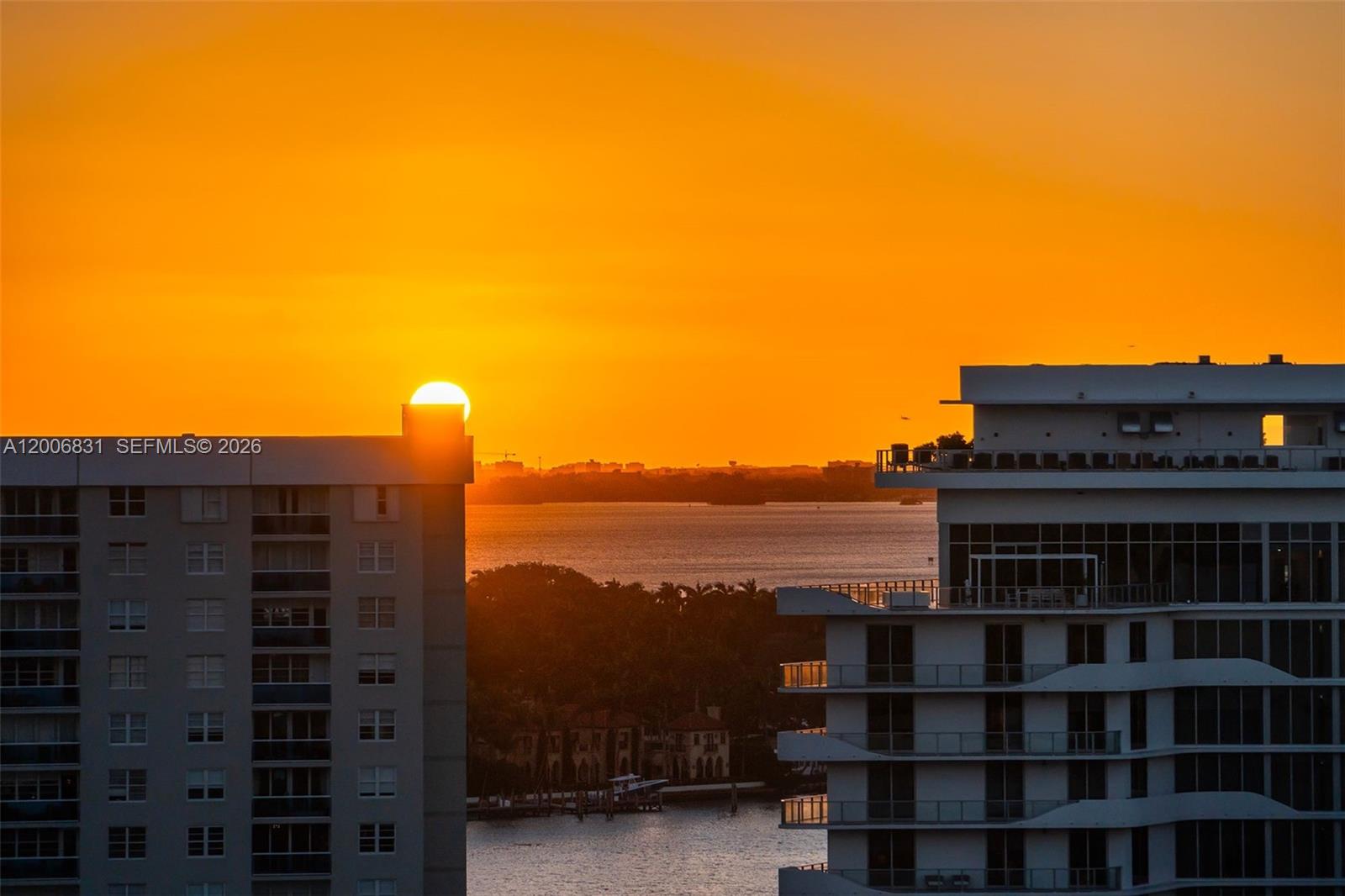 The sun sets behind two high-rise apartment buildings overlooking a body of water — 6801 Collins Ave, Miami Beach FL 33141, MIAMI BEACH, FL