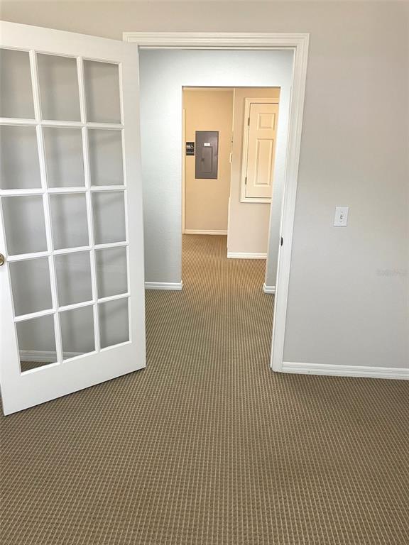 A room with beige carpet and a French door leads to a hallway with an electrical panel — 111 S RANDOLPH AVENUE, KISSIMMEE, FL