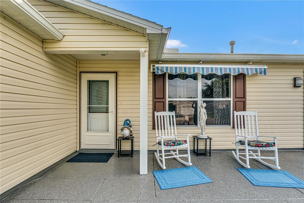 A covered front porch features light yellow siding, two white rocking chairs, and a door — 17654 SE 93RD BUTLER COURT, THE VILLAGES, FL