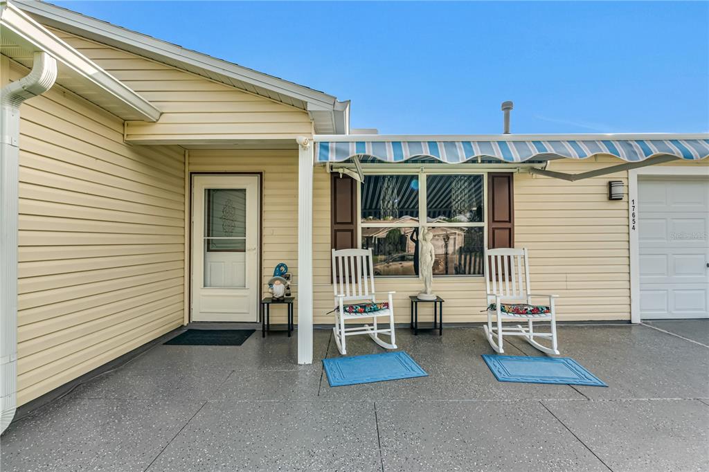 A covered patio with two rocking chairs sits in front of a yellow-sided house — 17654 SE 93RD BUTLER COURT, THE VILLAGES, FL