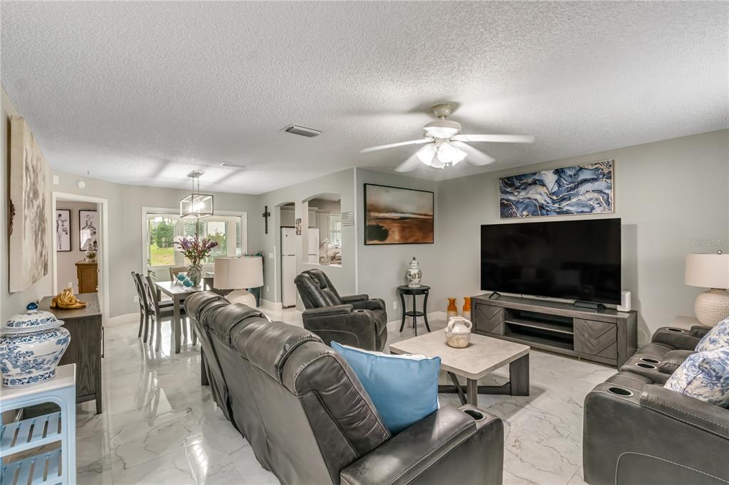 A living room with gray leather recliners, a television, and white marble-look tile flooring — 17654 SE 93RD BUTLER COURT, THE VILLAGES, FL