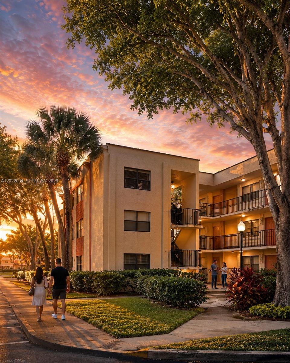 A multi-story apartment building exterior features balconies and a sidewalk with people at sunset — 3400 Foxcroft Rd # 301, Miramar FL 33025, MIRAMAR, FL