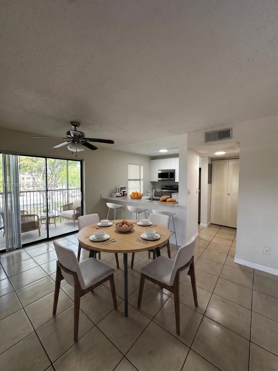 A dining area with a round table and chairs sits adjacent to a kitchen with bar seating — 3400 Foxcroft Rd # 301, Miramar FL 33025, MIRAMAR, FL