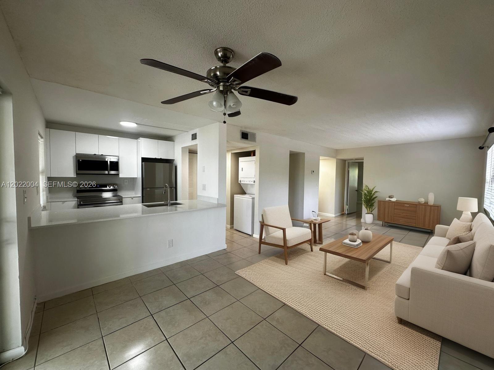 An open-concept living room and kitchen featuring tile floors, white cabinetry, and neutral furniture — 3400 Foxcroft Rd # 301, Miramar FL 33025, MIRAMAR, FL