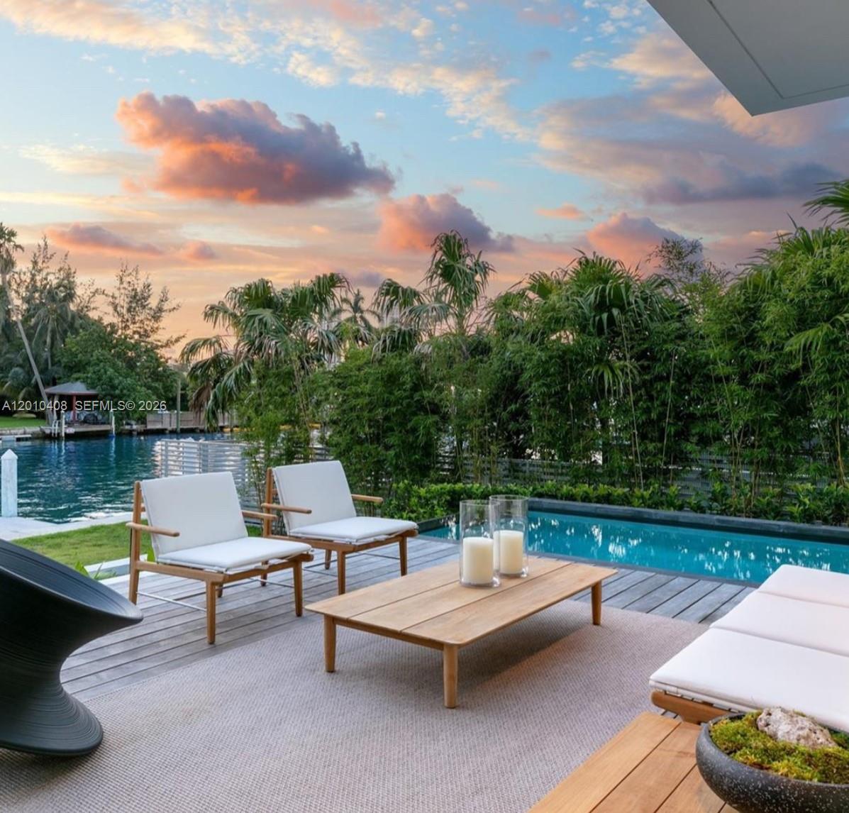 A patio with lounge chairs and a coffee table overlooks a swimming pool and canal — 1081 W 48th St # N01, Miami Beach FL 33140, MIAMI BEACH, FL