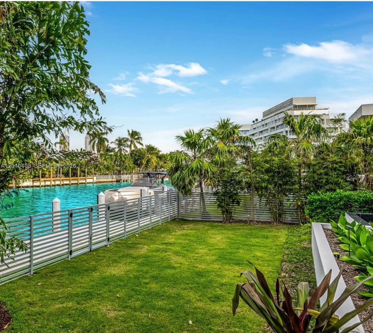 A grassy backyard features a metal fence overlooking a canal with a docked boat — 1081 W 48th St # N01, Miami Beach FL 33140, MIAMI BEACH, FL