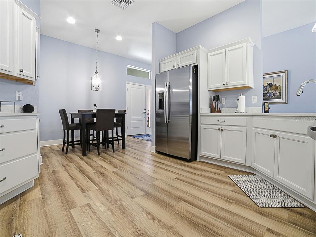 A kitchen with white cabinets, stainless steel appliances, and wood-look flooring next to a dining area — 4258 WIDMANN PLACE, THE VILLAGES, FL