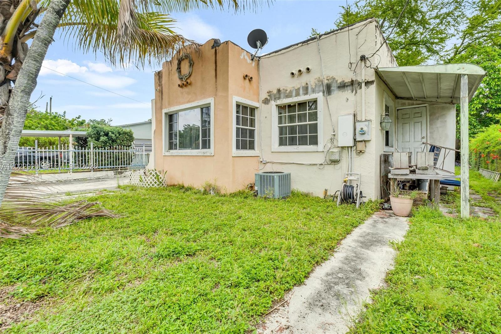 A small, weathered single-story house with a peach-colored facade and a metal porch awning — 1122 NW 38th St, Miami FL 33127, MIAMI, FL