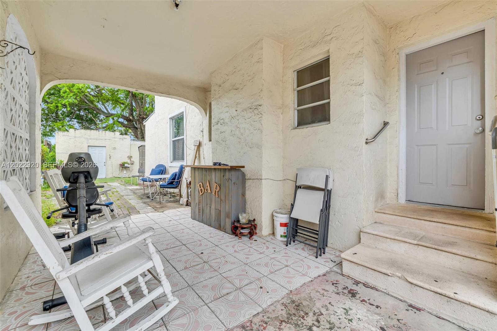 A covered patio features tiled flooring, a small wooden bar, and a set of stairs — 1122 NW 38th St, Miami FL 33127, MIAMI, FL